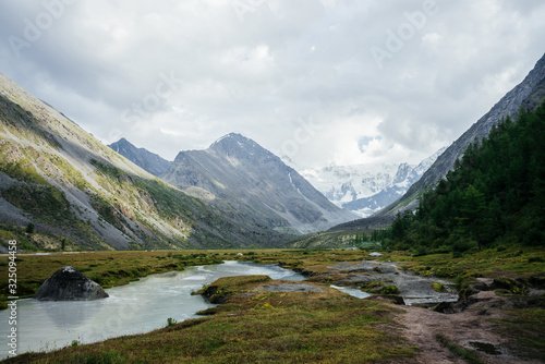 Awesome alpine view to mountain lake and great glaciers under gloomy sky. Dark atmospheric highland scenery with high snowy mountains and big rocks. Wonderful mountain landscape in cloudy weather.