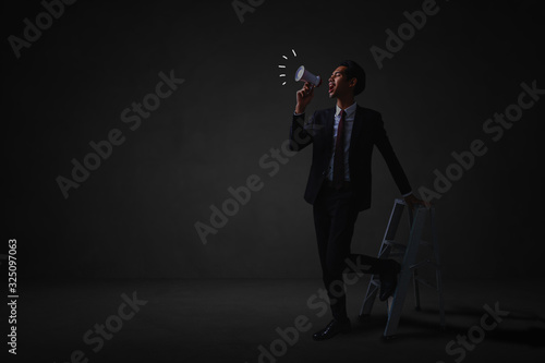 businessman standing and announce with megaphone to public relations in dark room