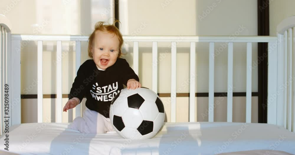Caucasian baby playing with football ball in bed. RAW Graded footage 4K slow motion 50fps Caucasian baby playing with football ball in bed. RAW Graded footage 4K slow motion 50fps