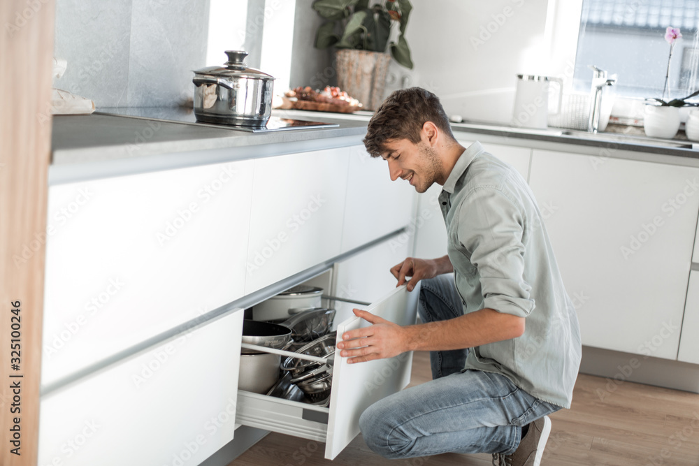 young man sitting near the dishwasher in his kitchen young man sitting near the dishwasher in his kitchen