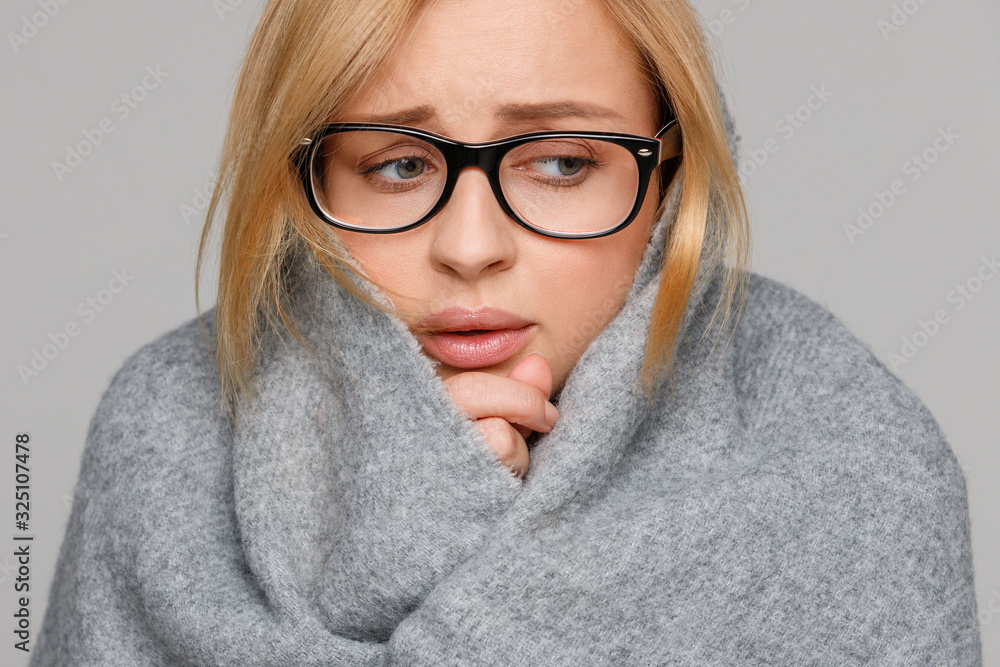 Upset business woman in glasses wrapped in warm scarf, caught a cold, looking down, isolated on grey background. First signs of flu/influenza. 