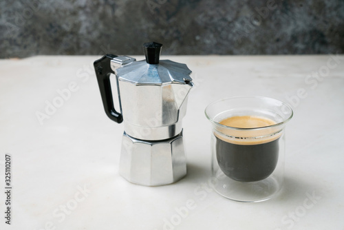 Moka pot with glass of fragrant coffee on the marble background. Side view.