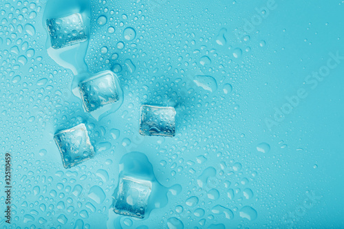 Ice cubes with water drops scattered on a blue background  top view.