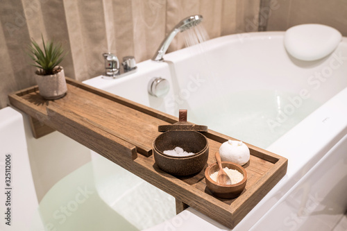 Obraz na płótnie Modern and comfortable bathroom, Bath tub with wooden table and toiletries, Salt, Herb, Bath Bomb