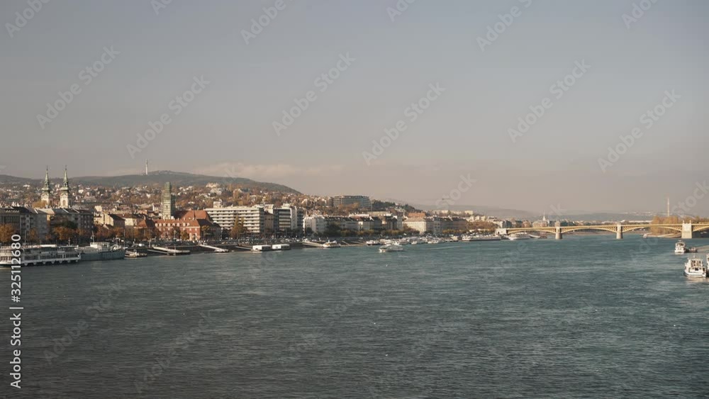 Gimbal shot of wide angle view of two sides of Budapest shot, from the bridge with view on Hungarian Parliament. Cloudy orange grey sky and boats of the river Danube Gimbal shot of wide angle view of two sides of Budapest shot, from the bridge with view on Hungarian Parliament. Cloudy orange grey sky and boats of the river Danube