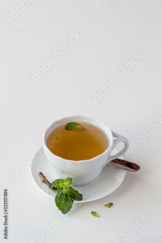 White porcelain cup with fragrant tea and fresh green mint leaves on a light background with copy space. Selective focus.