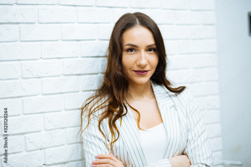 beautiful young business woman brown-haired in white clothes with a clear look near the white stone wall beautiful young business woman brown-haired in white clothes with a clear look near the white stone wall