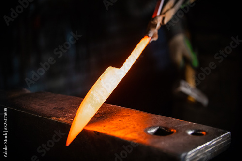 Fotografia Forging a knife out of the hot metal - holding the knife in forceps