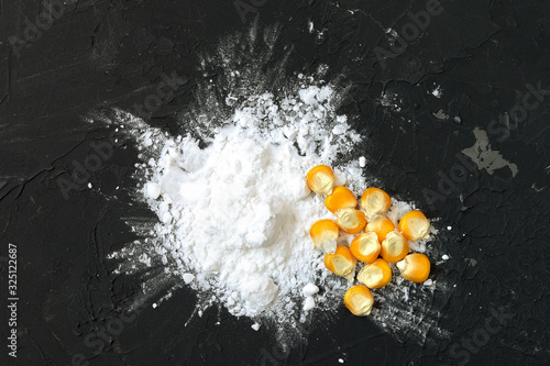 Corn starch with yellow grains on a black background, top view. Corn white starch and yellow kernels on the table. Starch and corn grains on a black background, top view. photo