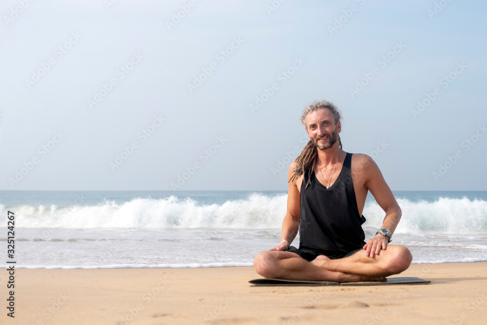 A man with dreadlocks on his head does yoga on the beach overlooking the ocean. Sri Lanka.