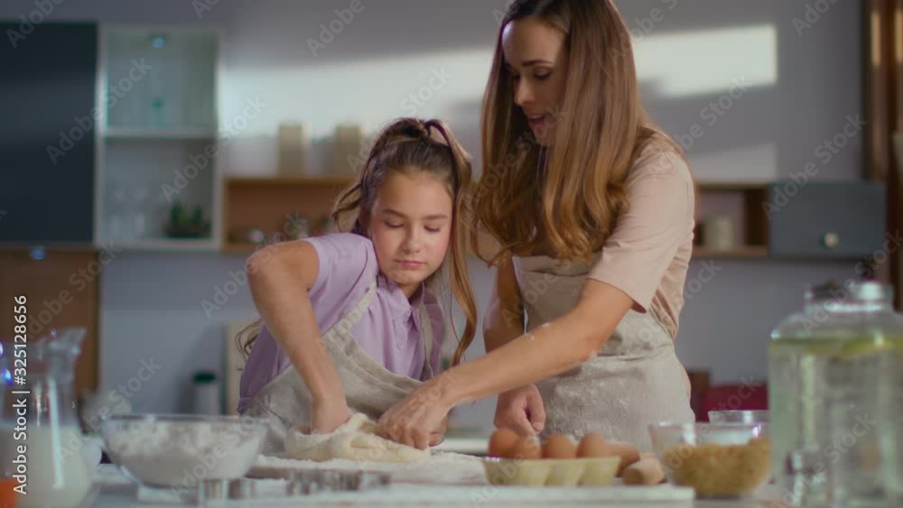 Mother teaching daughter to knead dough for cookies on kitchen in slow motion Mother teaching daughter to knead dough for cookies on kitchen in slow motion