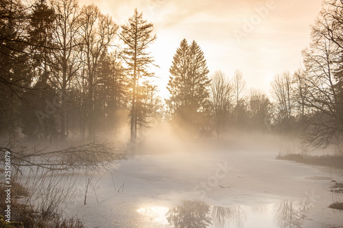 Misty sunset at the frozen pond after the rain in early spring with surrounding trees in Latvia
