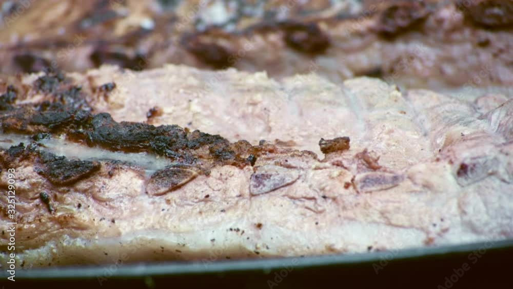 A close up of raw pork ribs being seasoned as they start to cook over a charcoal barbecue. A close up of raw pork ribs being seasoned as they start to cook over a charcoal barbecue.