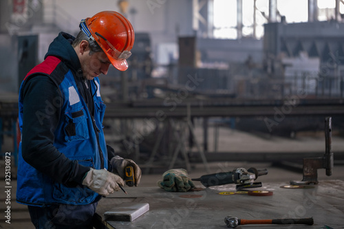 Billede på lærred The builder measures the stainless steel profile at the workplace in the production shop, measuring the desired size makes a mark with a pencil