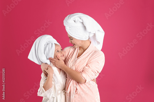 Happy mother and little daughter wearing bathrobes on pink background