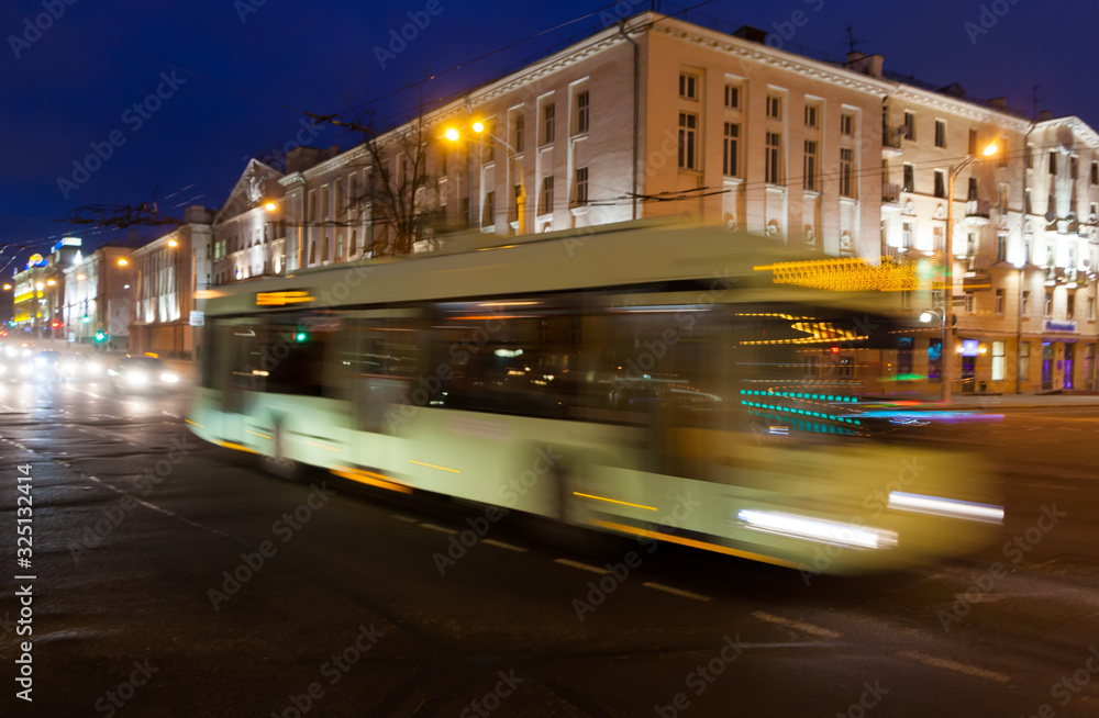 Motion blurred trolley bus along the street in the evening.