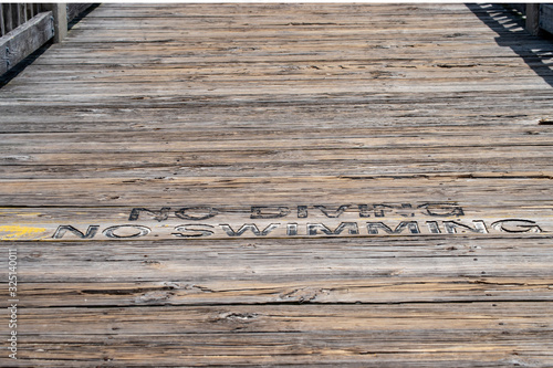 The wooden deck of a pier at the ocean in Mississippi is used as a sign board telling everyone that swimming and diving is not allowed. Bokeh.
