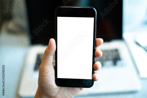 hand holding a mobile phone with white blank screen over the laptop