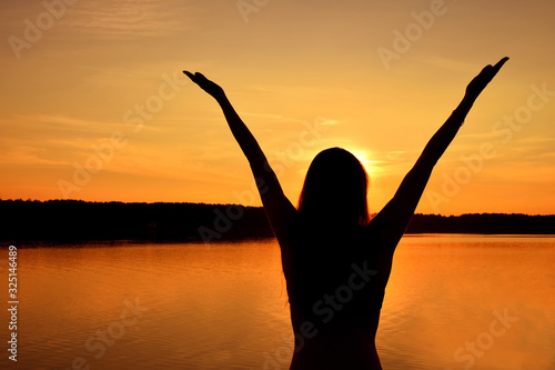 Silhouette of young woman over sunset sky and lake