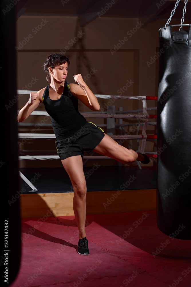 A young Caucasian woman actively trains in the gym and do boxing exercises in boxing gloves in front of a punching bag