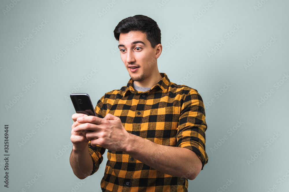 totally surprised man in yellow square shirt looking into the phone on grey background totally surprised man in yellow square shirt looking into the phone on grey background