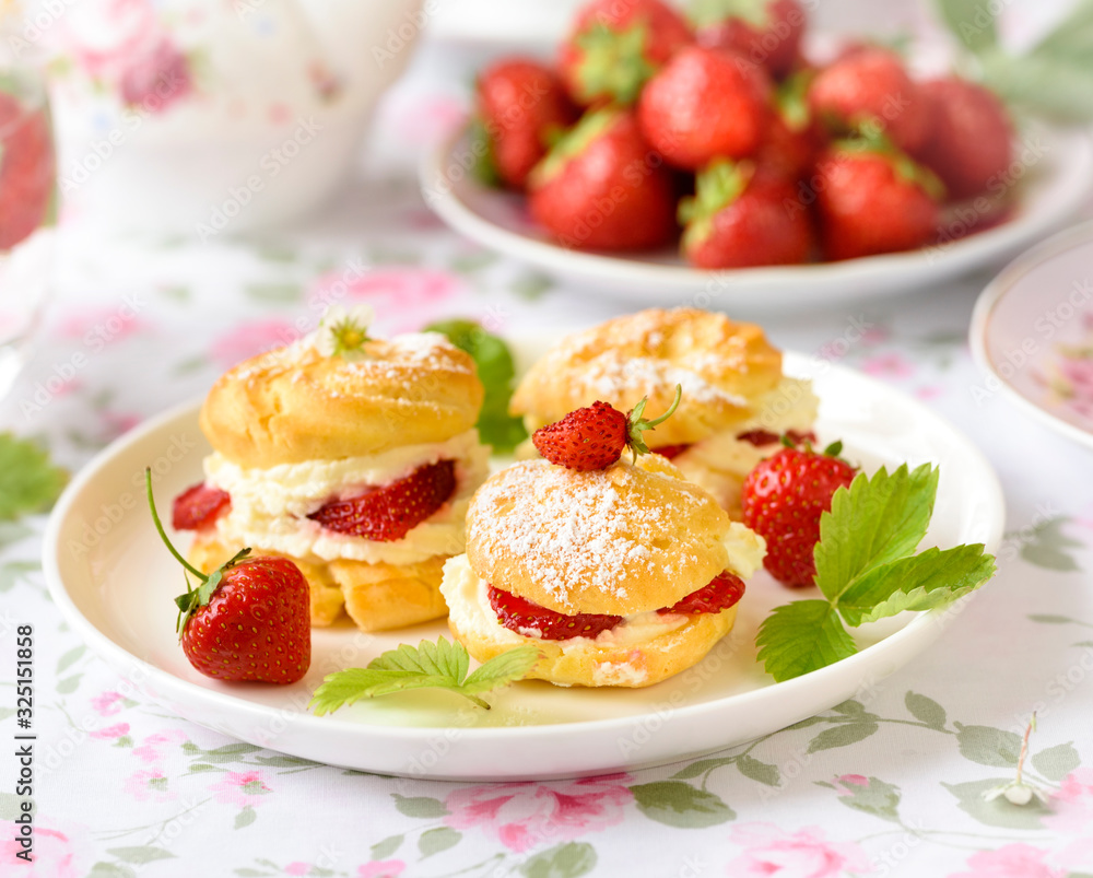 Profiterole or cream puff cakes filled with whipped cream, served with strawberries Profiterole or cream puff cakes filled with whipped cream, served with strawberries