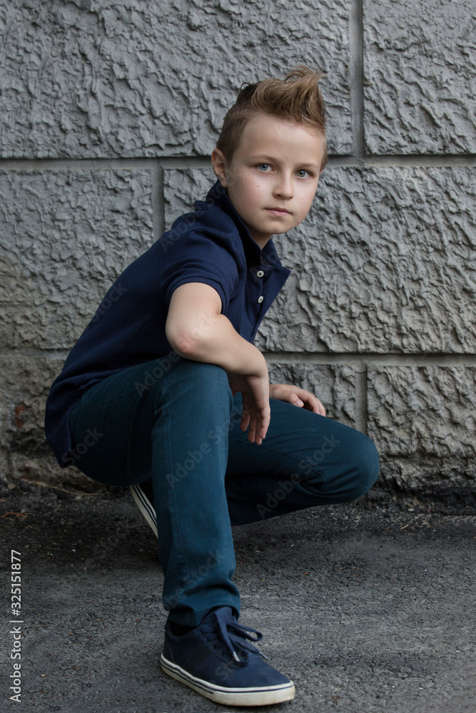 Handsome stylish boy sitting near a wall on the street. The boy has one eye blue, the other green. He is 13 years old. Handsome stylish boy sitting near a wall on the street. The boy has one eye blue, the other green. He is 13 years old.