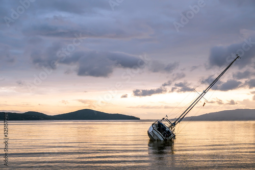 A lpneley sailing boat lying stranded in quite waters. Sea reflects cloudy sky at sun set