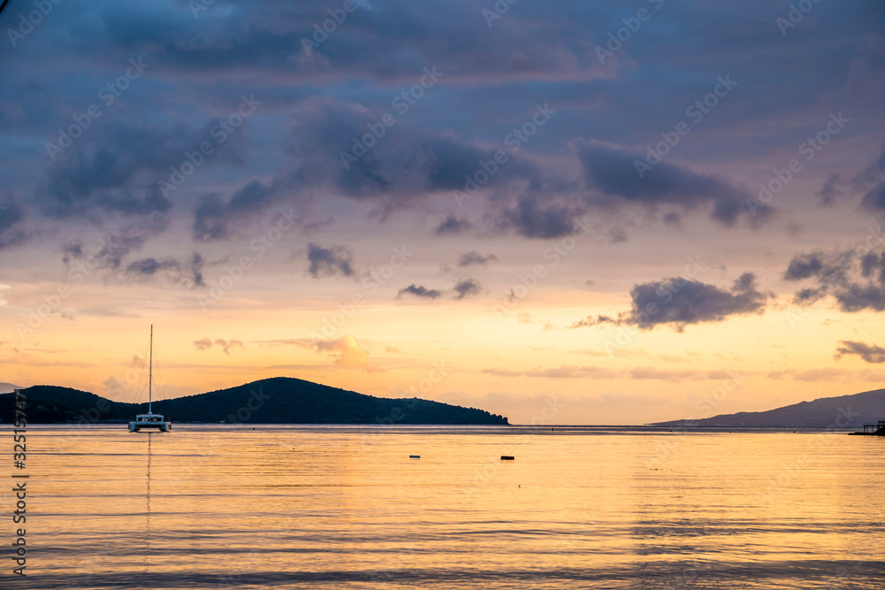 A single catamaran at a quite bay during sun set. Sea reflecting colors of cloudy sky A single catamaran at a quite bay during sun set. Sea reflecting colors of cloudy sky