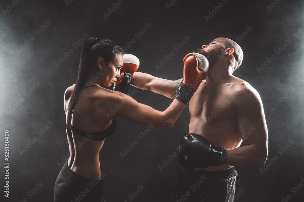 Fototapeta Shirtless Woman exercising with trainer at boxing and self defense lesson, studio, dark background. Female and male fight.