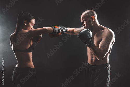 Shirtless Woman exercising with trainer at boxing and self defense lesson, studio, dark background. Female and male fight. © zamuruev