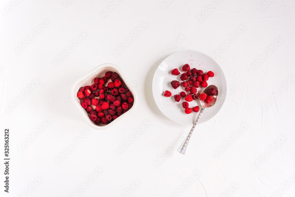Plate with a silver spoon and a container with raspberries on a white background. Fresh summer berries. Plate with a silver spoon and a container with raspberries on a white background. Fresh summer berries.