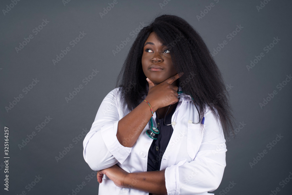 Isolated portrait of stylish young European woman with hand under chin and looking sideways with doubtful and skeptical expression, worry and doubt. Standing indoors over gray background. Isolated portrait of stylish young European woman with hand under chin and looking sideways with doubtful and skeptical expression, worry and doubt. Standing indoors over gray background.