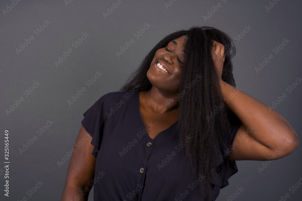 Shot of happy young African American woman with positive smile, has long hair, rejoices having weekend and good rest after hard working exhausting week, isolated on gray wall. Shot of happy young African American woman with positive smile, has long hair, rejoices having weekend and good rest after hard working exhausting week, isolated on gray wall.