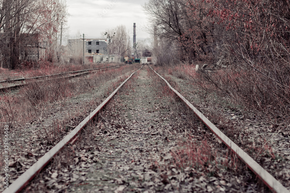 Railroad tracks to an old abandoned factory. The railway tracks. Landscape with railroad leading lines Railroad tracks to an old abandoned factory. The railway tracks. Landscape with railroad leading lines