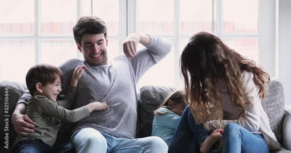 Cheerful parents and kids look at camera tickling on sofa Cheerful parents and kids look at camera tickling on sofa