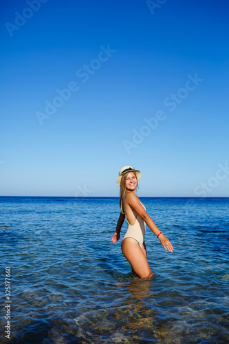 girl in a light hat and a beige swimsuit splashes in the blue water of the Red Sea