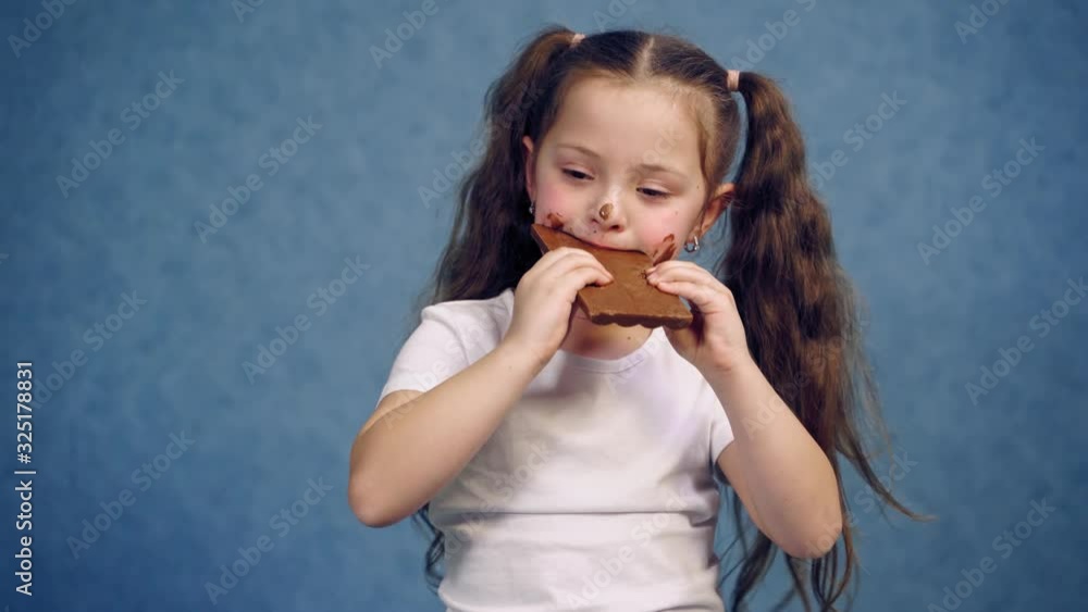 Dirty girl eating chocolate. Funny child holding a bar of chocolate and biting a piece of sweet isolated in studio. Joyful childhood. Dirty girl eating chocolate. Funny child holding a bar of chocolate and biting a piece of sweet isolated in studio. Joyful childhood.