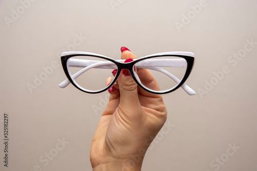 A woman's hand holds glasses, selection of glasses to improve vision on a gray background, recommendations of ophthalmologists and optometrists, optics and frames.