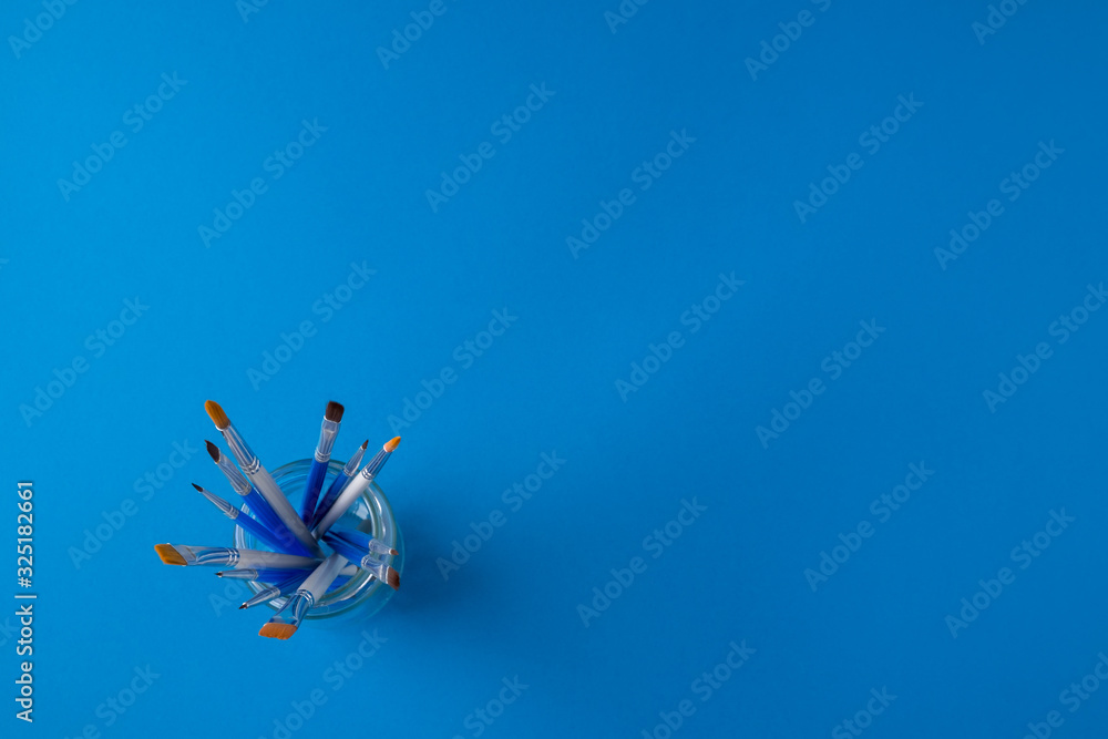 Flay lay, top view table desk. Set of different artist brushes in a glass stand on a blue background. copy space