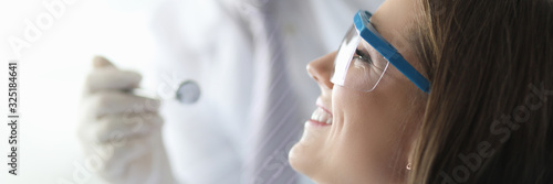 Close-up of smiling beautiful woman visiting professional stomatologist. Wonderful female with long brunette hair wearing special glasses. Healthcare and dentist photo