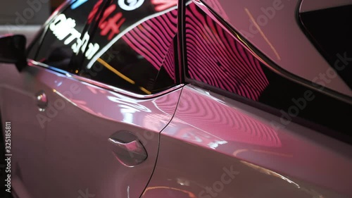 White clean, shiny, new car with pink, blue, red, white highlights and reflections on the doors and tinted windows stands at night in the parking lot of the shopping center