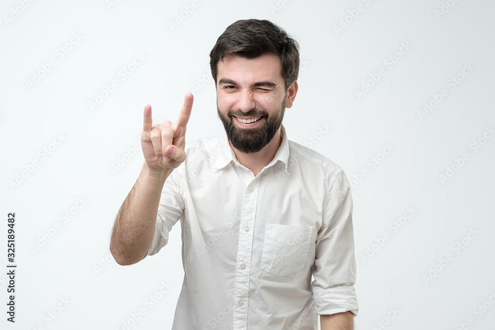 Young man showing rock sign with his fingers as if listening to favourite music Young man showing rock sign with his fingers as if listening to favourite music