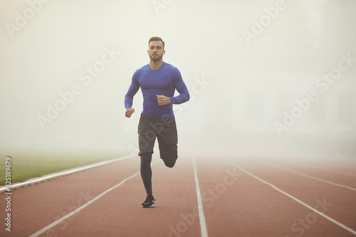 A young athlete runs on a stadium in the fog. © Studio Romantic