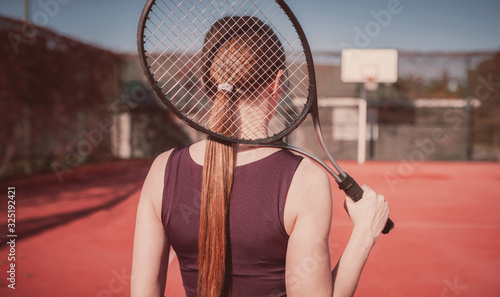 Beautiful and slender girl with a racket plays tennis, girl stands with her back to the viewer © Egor