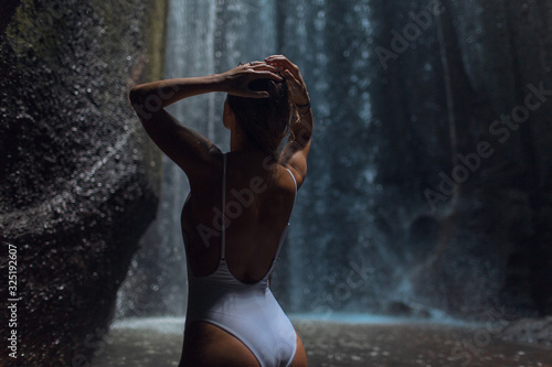 Beautiful young girl in a swimsuit near a tropical waterfall.