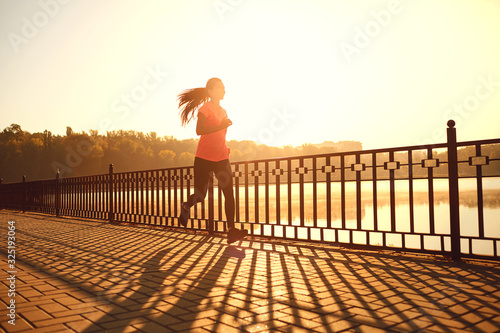 Girl runner runs in a park by the lake at dawn photo