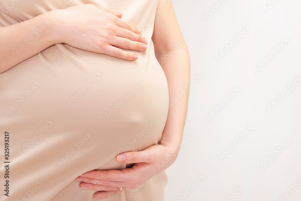 pregnant woman in a dress holds her hands on her stomach on a light background. Pregnancy, motherhood, preparation and expectation concept. Close-up indoors. Beautiful tender mood photo pregnancy.