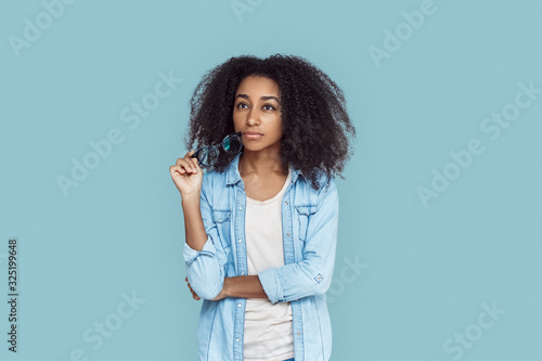 Freestyle. African girl standing isolated on gray with glasses looking aside pensive