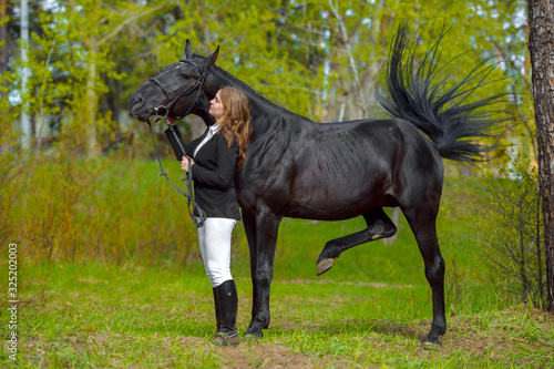 Young girl rider with a black horse in the spring